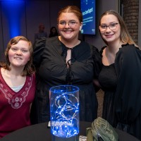 3 girls smiles together around table as they pose